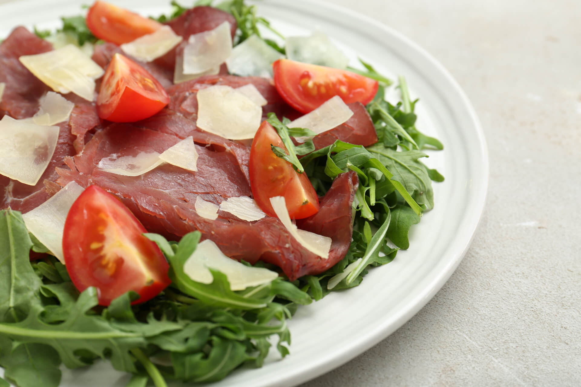 abbinamenti con la bresaola: piatto di bresaola con rucola grana a scaglie e pomodorini